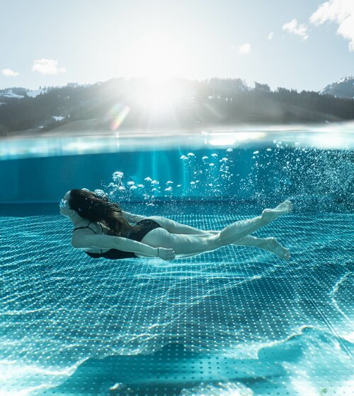 Frau schwimmt unter Wasser im Infinity Pool