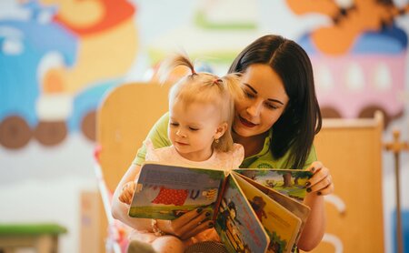 Kinderbetreuerin liest Kleinkind ein Buch vor